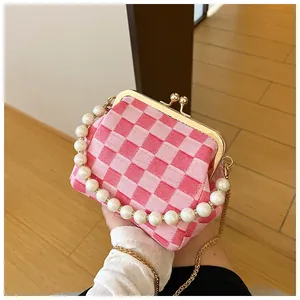 Detail van roze geruite crossbodytas met groot parelhandvat en gouden kettingriem