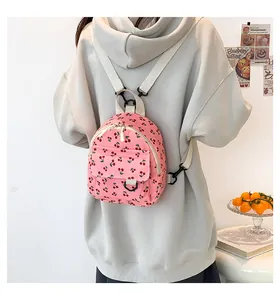 Pink corduroy mini backpack with red cherry print and ivory straps worn by a model