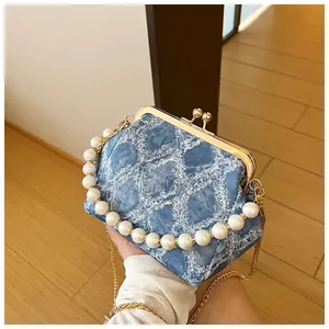 Detail van blauwe denim crossbodytas met parelhandvat en gouden sluiting
