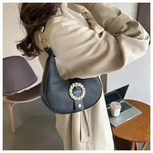 Detail of black crescent shoulder bag with golden round buckle in a cozy cafe setting