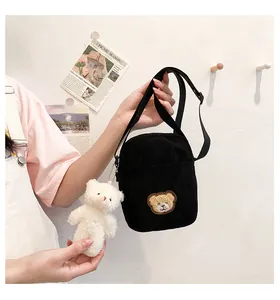 Detail of black corduroy shoulder bag featuring a cute plush bear patch and charm