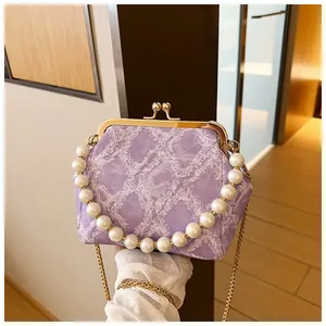 Detail van paarse stoffen handtas met parelhandvat en gouden metalen kettingriem