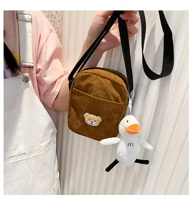 Detail of brown corduroy bear crossbody bag with a white duck plush charm attachment
