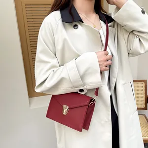 Minimalistische dunkelrote Umhängetasche mit Goldschnalle auf einem beigen Trenchcoat