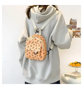 Detail of orange-pink corduroy mini backpack featuring cherry prints and white straps