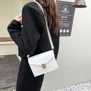 Minimalistische weiße Umschlag-Umhängetasche aus Leder mit goldenem Verschluss am Model