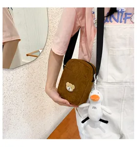 Detail of brown corduroy crossbody bag with bear embroidery and plush duck charm