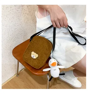 Detail of tan corduroy crossbody bag featuring a bear patch and a plush duck charm