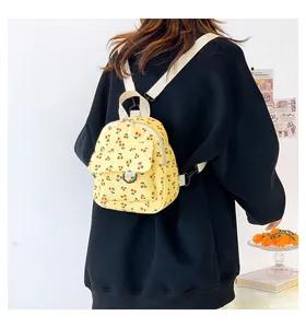 Detail view of yellow corduroy backpack with red cherry print on a female model back