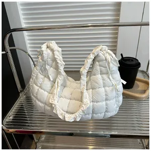 Détail du sac matelassé blanc avec poignée à volants posé sur un support métallique