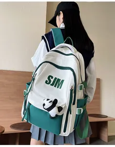 Detalle de la mochila escolar grande blanca y verde con letras SJM y peluche de panda