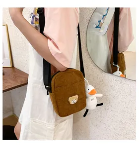 Detail of brown corduroy crossbody bag with teddy bear patch and duck plush charm