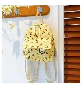 Detail of a bright yellow corduroy mini backpack with cherry prints hanging on a hook