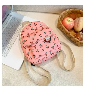 Pink corduroy mini backpack with cherry print next to a picnic basket and laptop