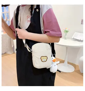 Close-up of off-white corduroy crossbody bag with brown bear patch and duck charm