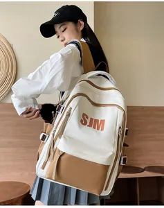 Detalle de mochila bicolor con logo SJM, hebillas laterales y colgante de peluche negro