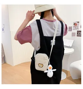Detail view of beige corduroy crossbody bag with bear patch and plush duck charm accessory