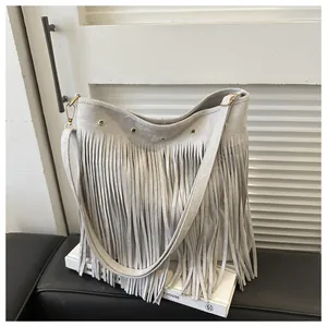 Close-up detail of light gray bohemian fringe shoulder bag with metal eyelets and suede texture