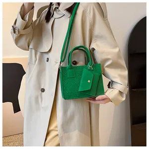 Detail of green embossed felt handbag with crossbody strap on a beige trench coat