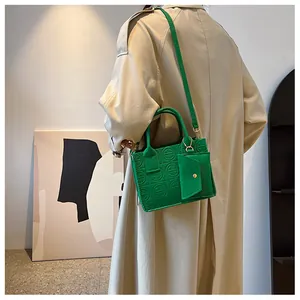 Detail of green embossed felt tote bag with small matching pouch shown on a model