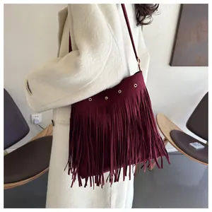Detail of wine red fringe shoulder bag with metal eyelets and suede texture on white coat