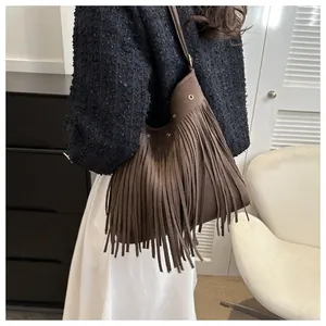 Close-up of brown suede fringe bag with metal eyelets worn by a model in boho style