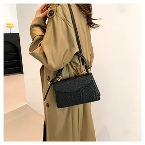 Borsa a tracolla intrecciata nera con patta a busta e manico annodato su cappotto beige