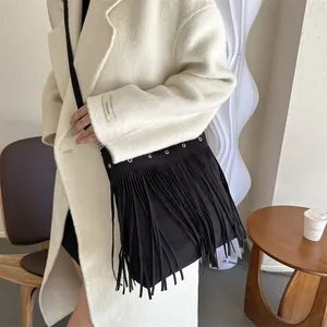Bohemian black fringe shoulder bag with metal eyelets worn over a cream cashmere coat