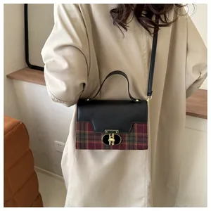 Detail view of red and green plaid crossbody bag with a gold lock on a beige trench coat