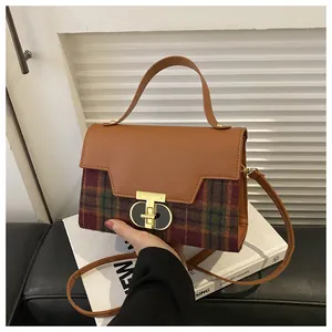 Detail of the golden dual-ring lock and brown leather handle on a plaid handbag