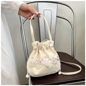 Detailed embroidery of pink flowers on a beige drawstring bucket bag with pearl accent