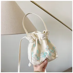 Detailed close-up of floral embroidery and pearl drawstring on beige canvas bucket bag