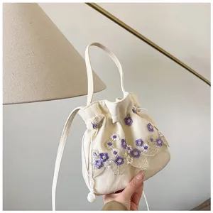 Close-up of floral embroidery and lace details on a cream-colored bucket bag with pearls