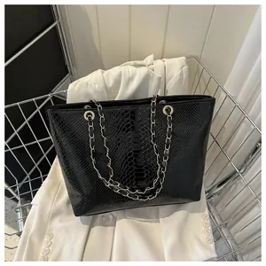 Detail of black tote bag with snakeskin texture and golden chain shoulder straps