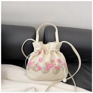 Detailed pink floral embroidery with gold accents and pearl drawstring on beige bag