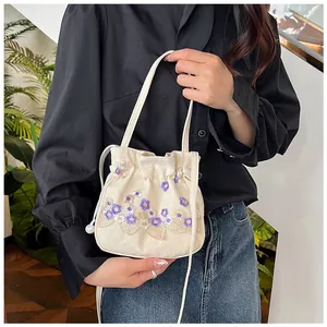 Detail of floral embroidery on cream canvas bucket bag with elegant pearl drawstring closure
