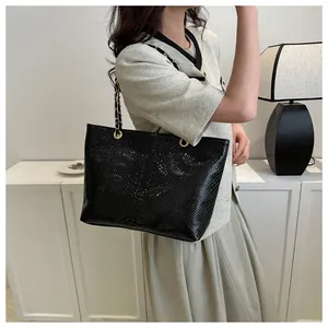Close-up of glossy crocodile pattern texture and gold chain strap on black tote bag