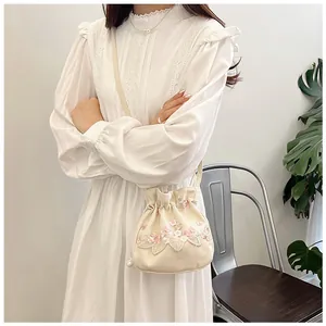 Close-up of white lace bucket bag with floral embroidery and pearl drawstring detail