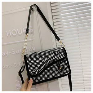 Detail of a black crossbody bag with rhinestones, a bear charm, and a pearl strap