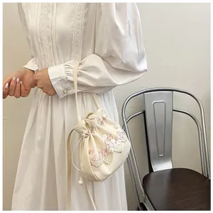 Detail of floral embroidery and pearl drawstring on beige handmade lace bucket bag