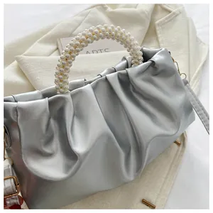 Nahaufnahme der silbernen Falten-Cloud-Tasche mit Perlengriff auf beigem Blazer