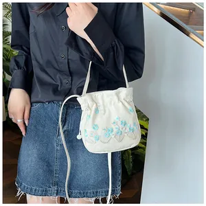 Close-up of cream canvas drawstring bucket bag with delicate blue flower embroidery detail