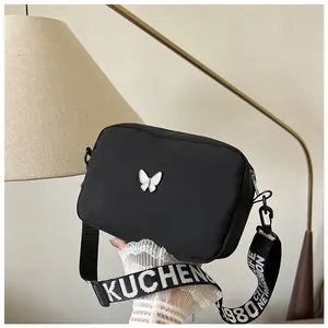 Détail du sac bandoulière noir en nylon avec papillon 3D blanc et large sangle lettrée
