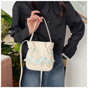 Detail of cream canvas bucket bag with floral embroidery and drawstring closure