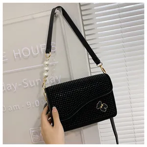 Detail of black crossbody bag with sparkling rhinestones, large pearls and gold bow logo