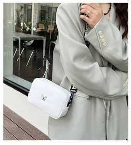 Détail du sac bandoulière en nylon blanc avec logo papillon argenté et sangle jacquard