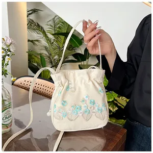 Detailed embroidery on a cream canvas bucket bag featuring floral patterns and drawstring