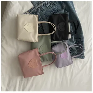 Flat lay of colorful nylon mini tote bags with heart smiley patches on white fabric