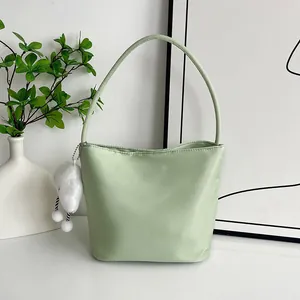 Hellgrüne Nylon-Eimertasche mit weißem Plüschherz-Anhänger in schlichter Umgebung