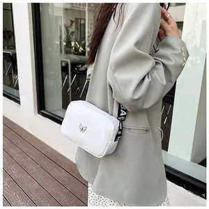Vue détaillée du sac bandoulière en nylon blanc avec papillon et large sangle tissée